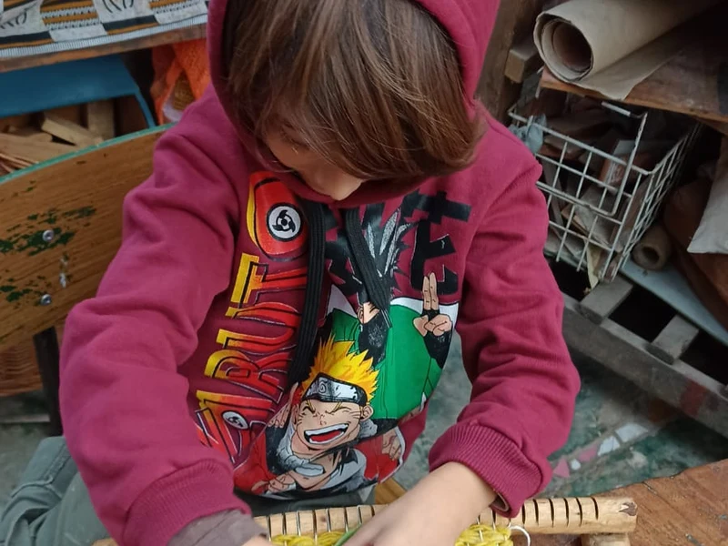 Niño tejiendo en telar de madera en KIFF